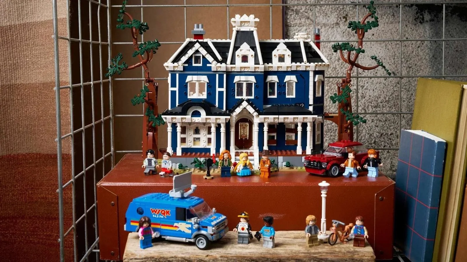 LEGO Stranger Things Creel House set shown as a pristine blue Victorian house, displayed on a vintage trunk