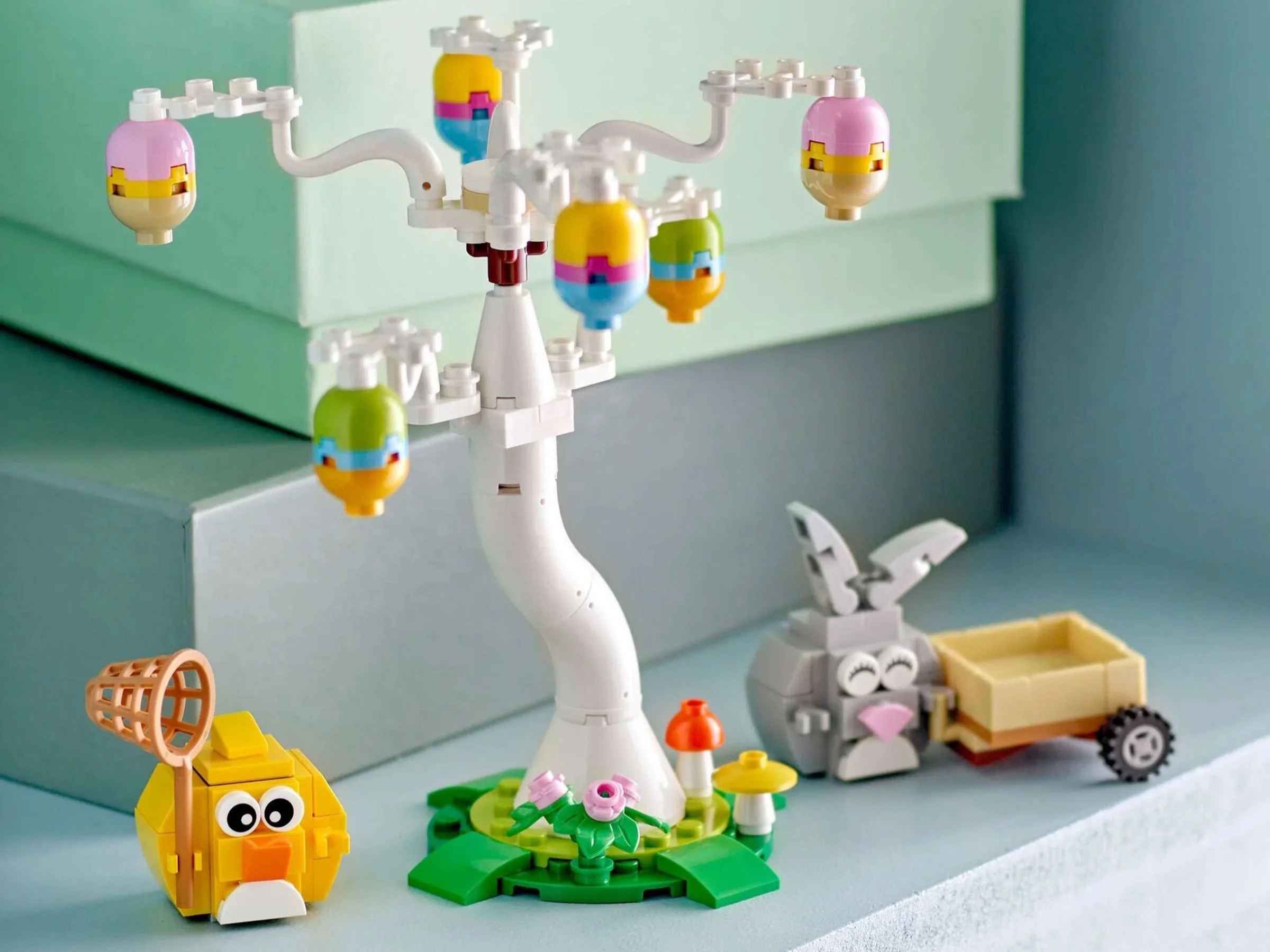 LEGO Easter Bunny and Chick Egg Hunt set with a white egg tree, gray bunny with a cart and yellow chick holding a net, styled on pastel boxes