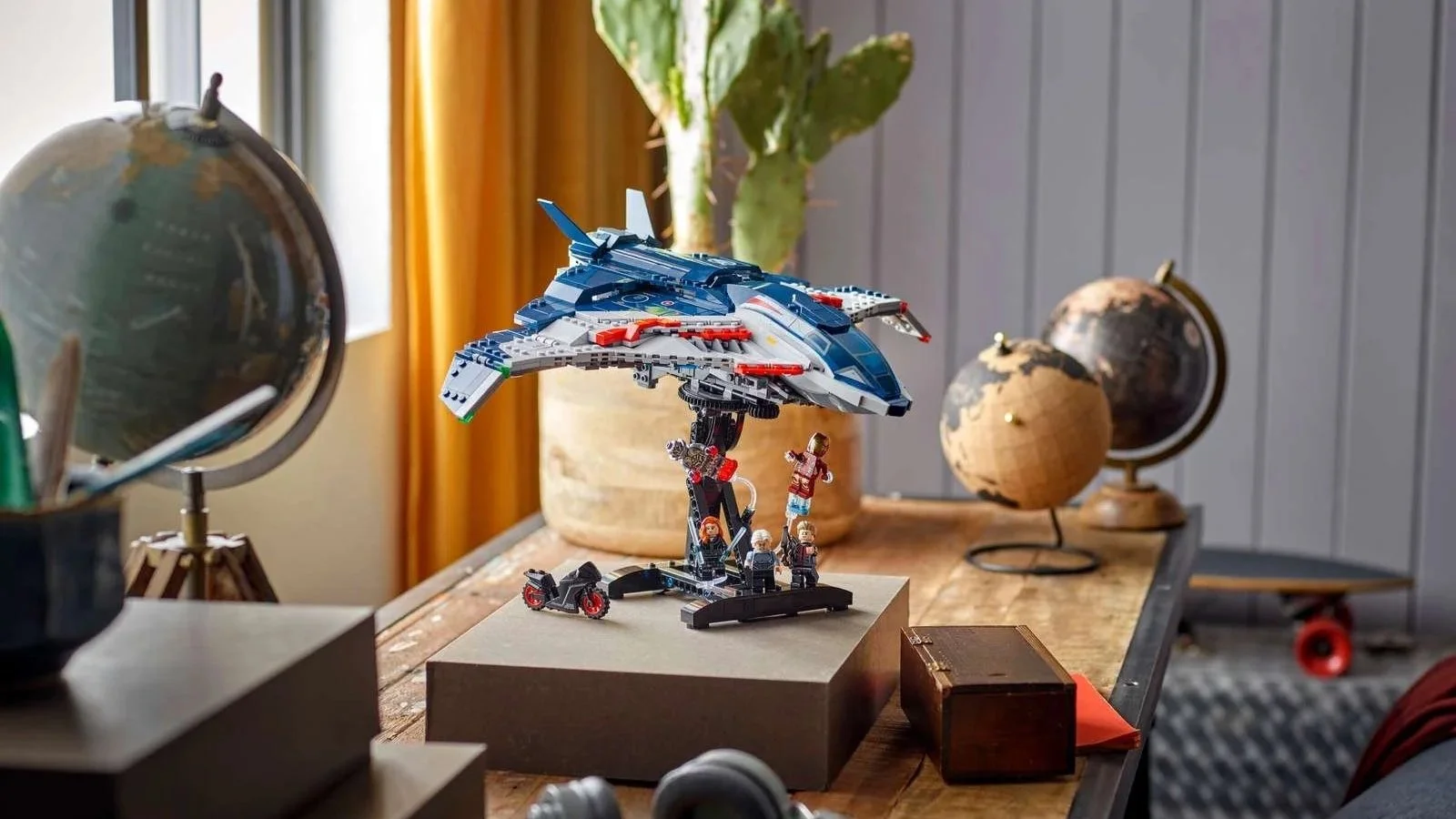 LEGO Marvel Avengers: Age of Ultron Quinjet on a black display stand on a wooden desk beside vintage globes and a cactus