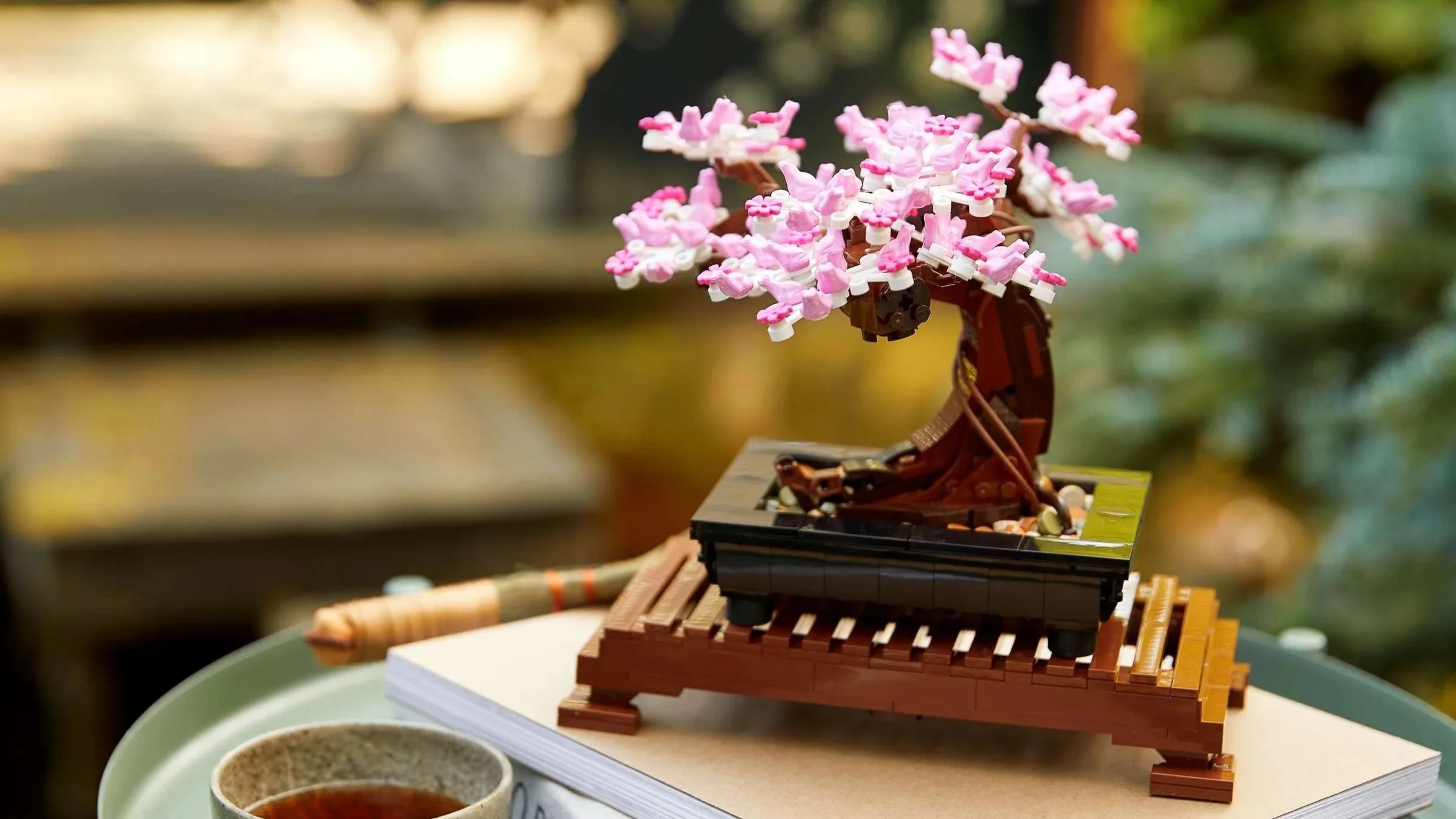 LEGO Bonsai Tree with pink cherry blossoms styled on stacked books beside a cup of tea in the garden