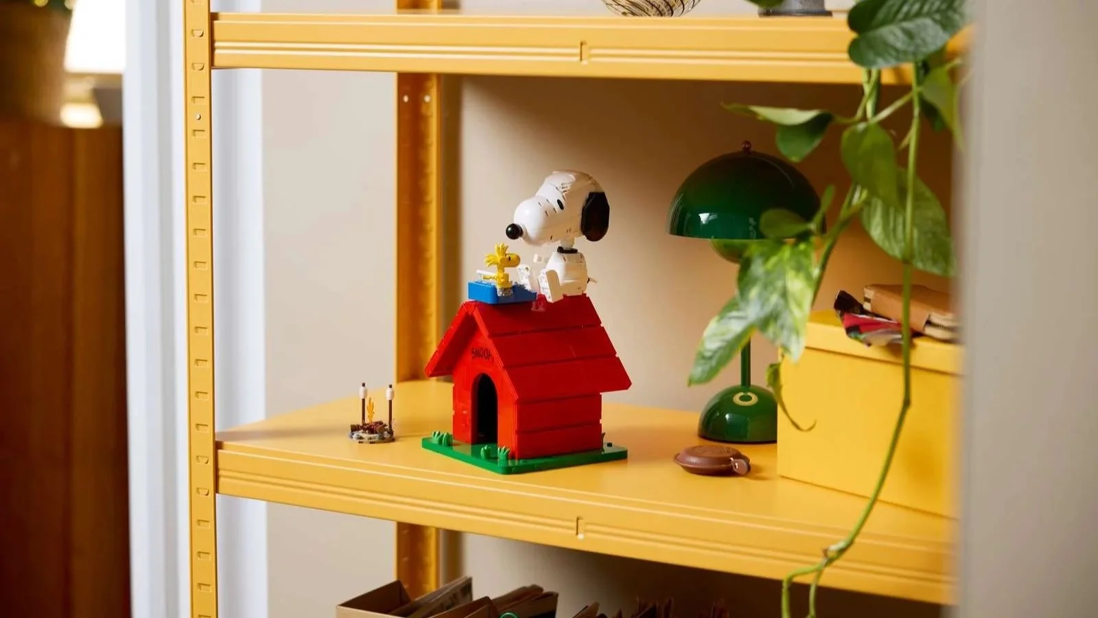 LEGO Peanuts Snoopy's Doghouse set with Snoopy and Woodstock on a yellow shelf beside a green lamp
