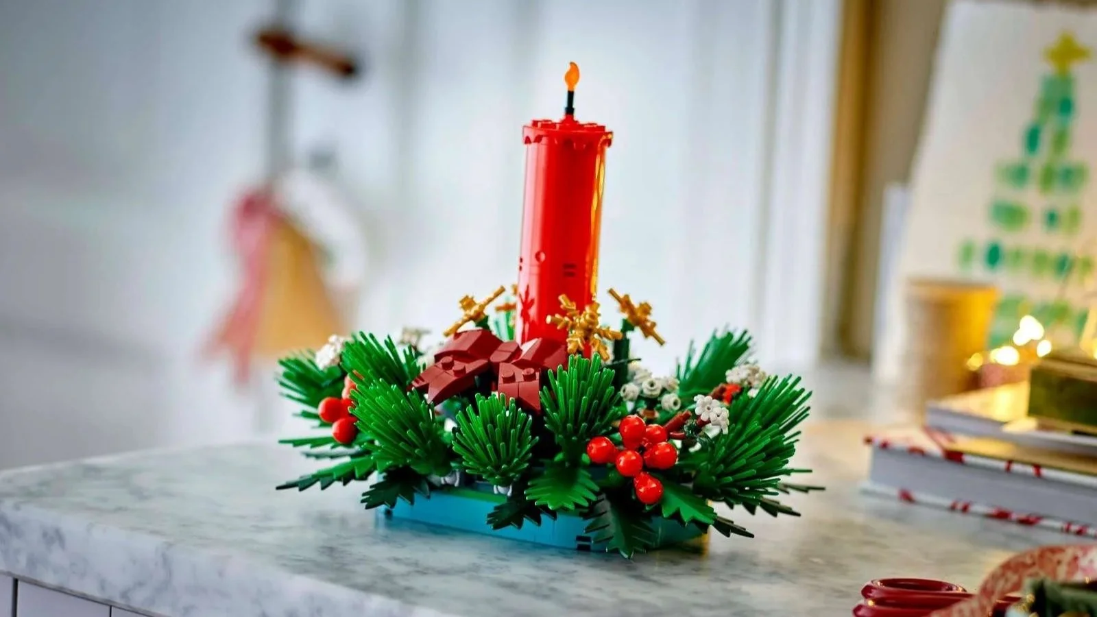 LEGO Christmas table decoration with a tall red candle, bow, gold snowflakes, pine sprigs and red berries on a marble counter
