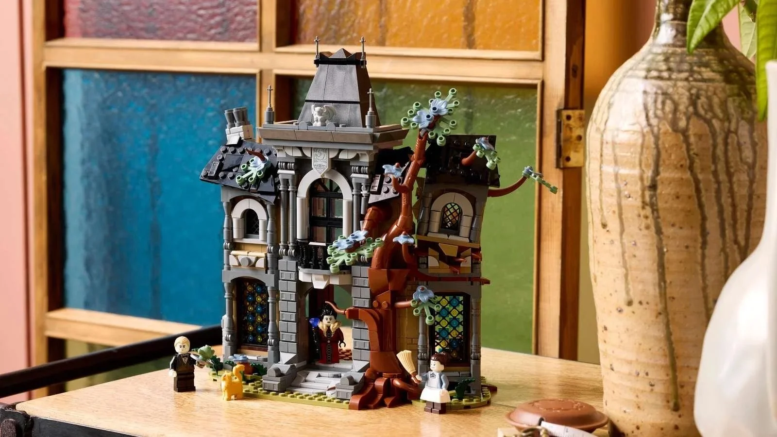 LEGO Mayor Manor set, a gray gothic mansion with a twisting brown tree, stained glass windows and three minifigures on a wooden table