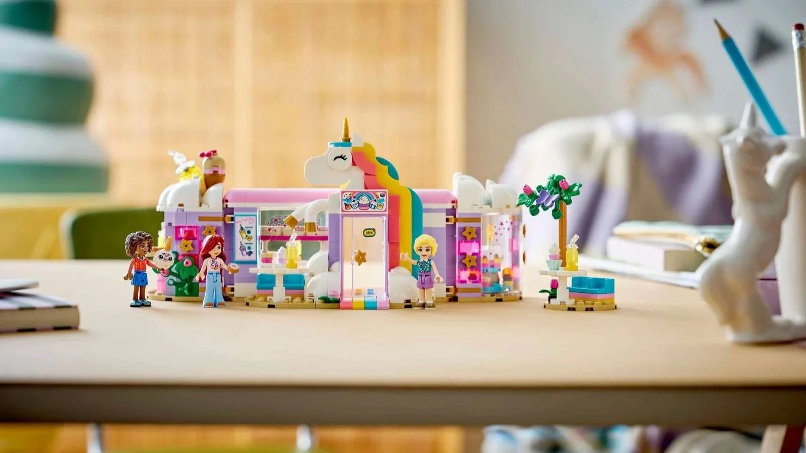 LEGO Unicorn Dream Café set on a desk, a lavender café with a white unicorn head and rainbow mane above the door, outdoor tables with treats and three figures