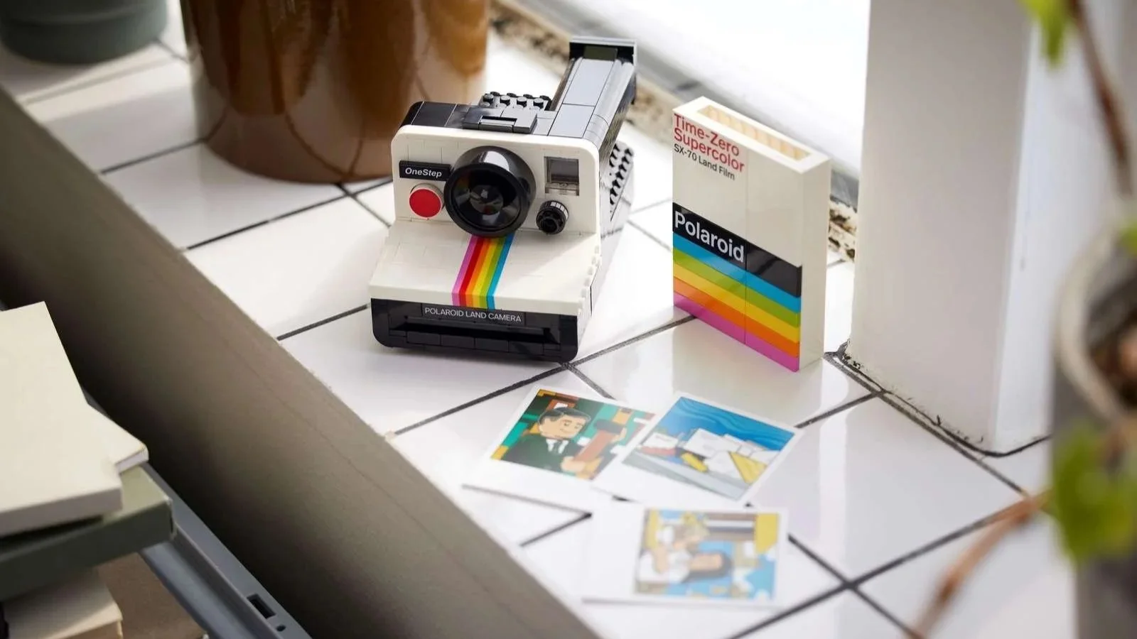 LEGO Polaroid OneStep SX-70 Camera set with a rainbow stripe, film box and instant photos on a white tiled windowsill