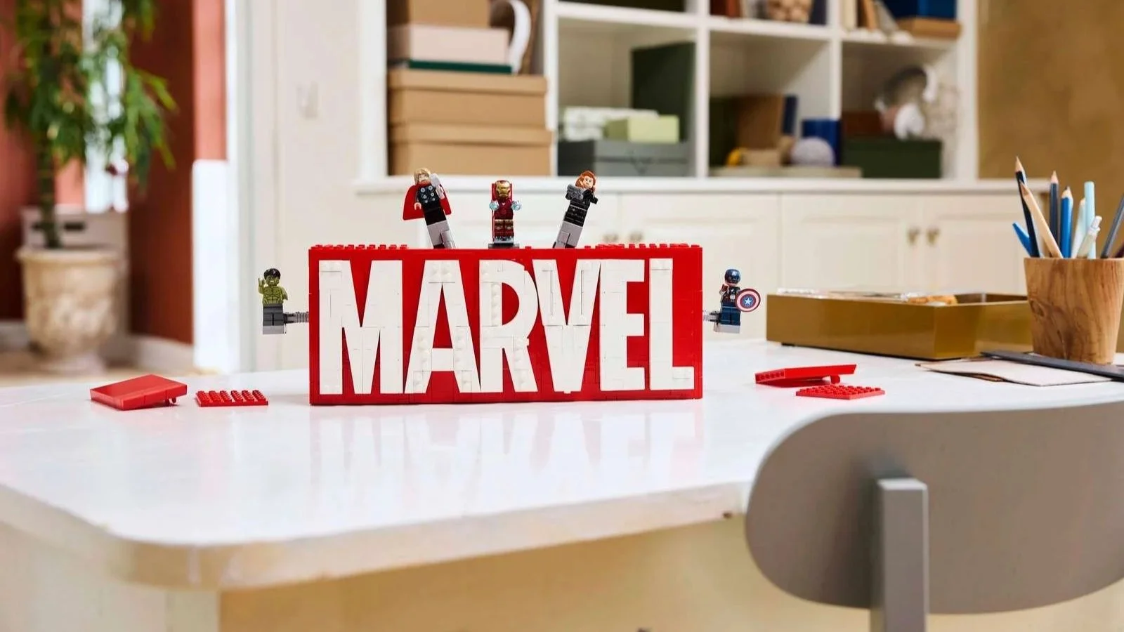 LEGO MARVEL Logo & Minifigures set with the Avengers climbing the brick-built red logo on a white craft table