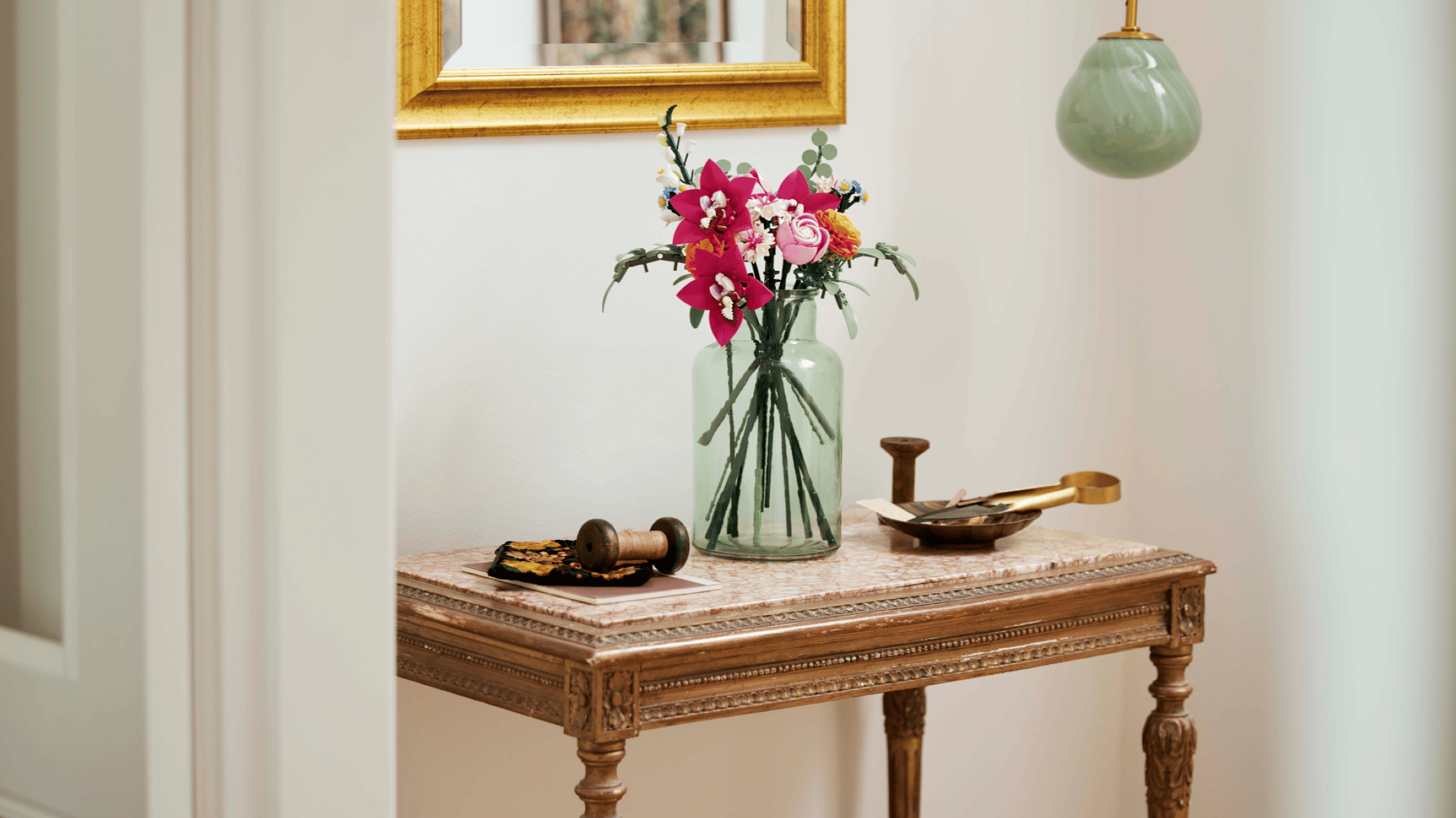 LEGO Pretty Pink Flower Bouquet set in a green glass vase on a marble-top console table beneath a gold-framed mirror