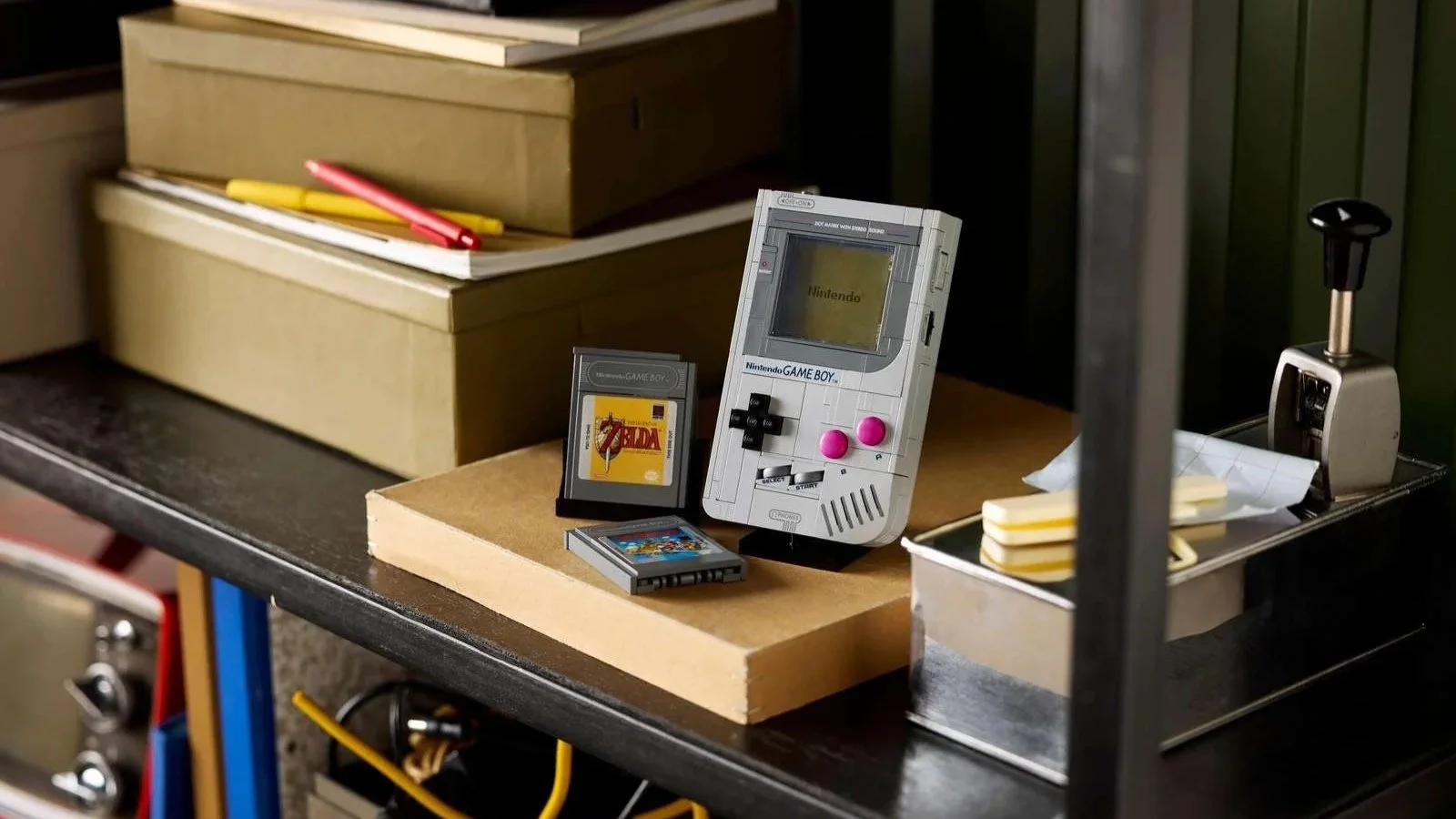 LEGO Game Boy set standing upright on a shelf, paired with a Zelda game cartridge among books and craft supplies