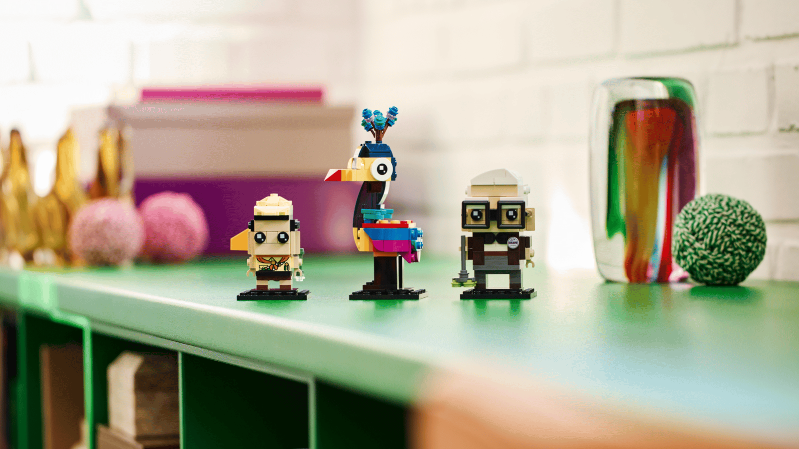 LEGO Carl, Russell and Kevin set with three buildable characters, a young scout, a colorful bird, and an elderly man in glasses, lined up on a green shelf