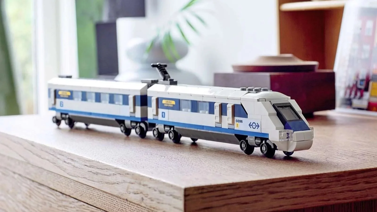 LEGO High-Speed Train set in white and blue with two connected cars, displayed on a wooden cabinet beside a plant