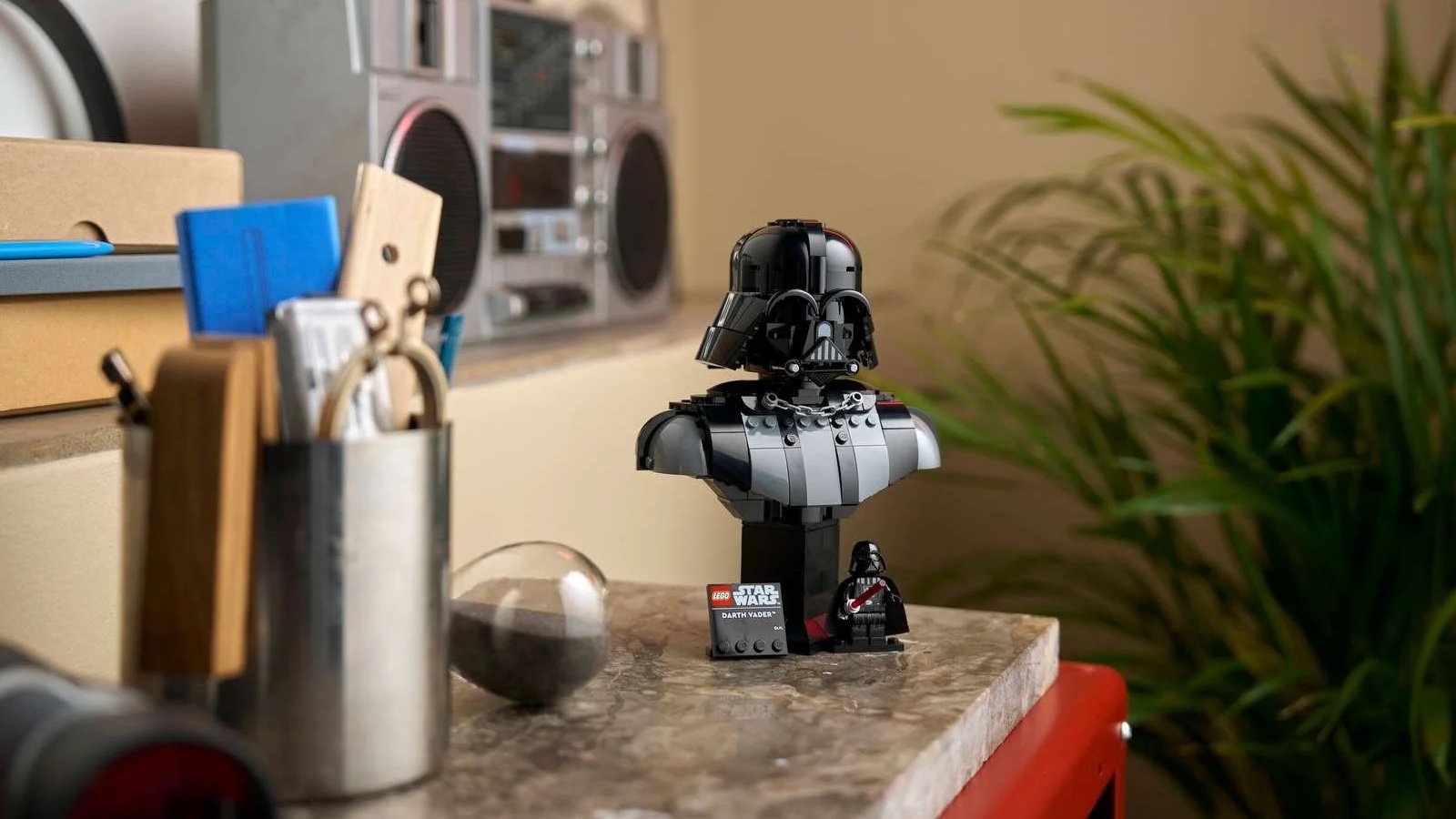 LEGO Star Wars Darth Vader Bust displayed on a marble counter beside a retro boombox and a leafy houseplant