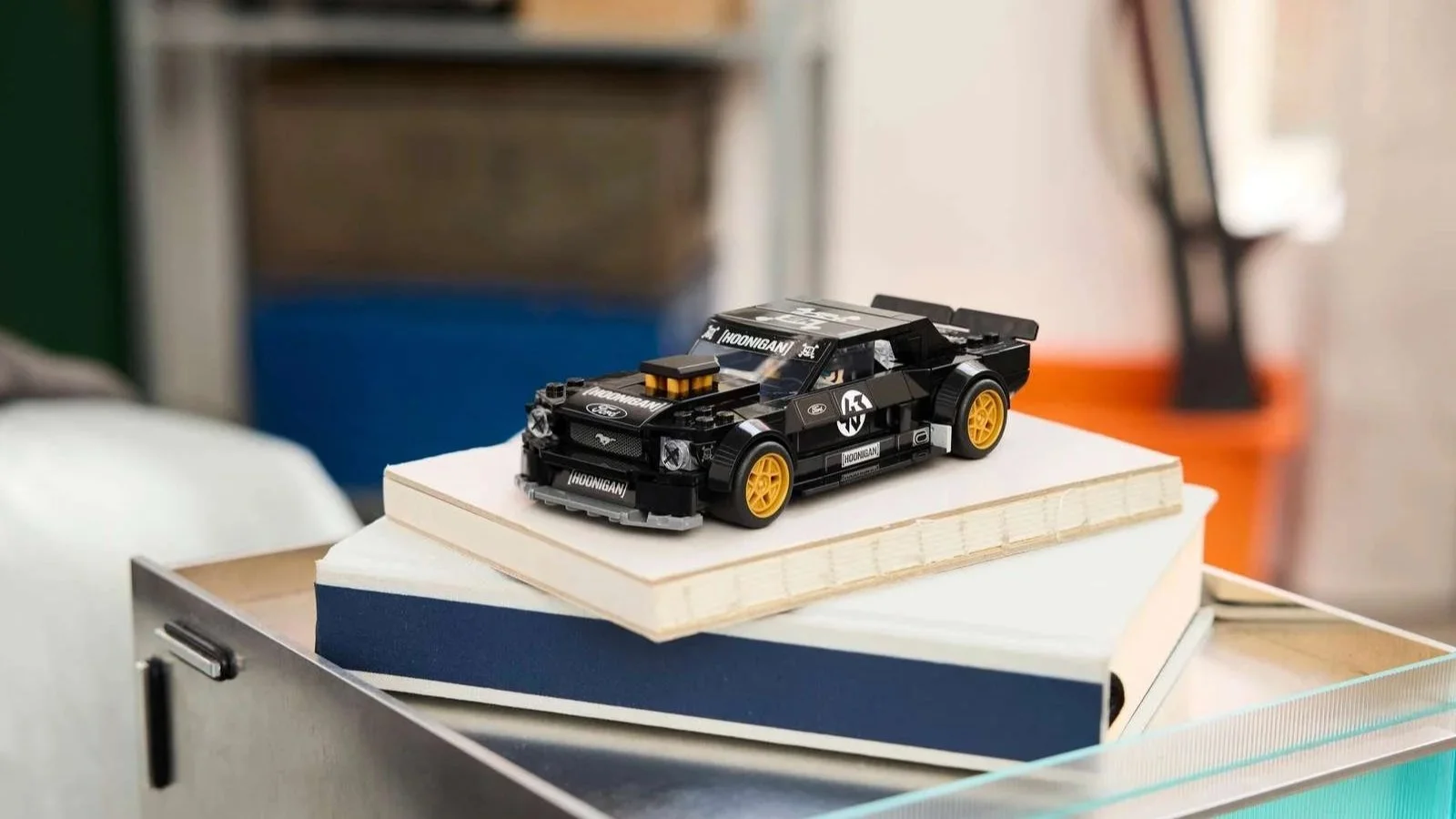 LEGO Ford Mustang Hoonicorn model car in black with Hoonigan branding, resting on a stack of books on a desk