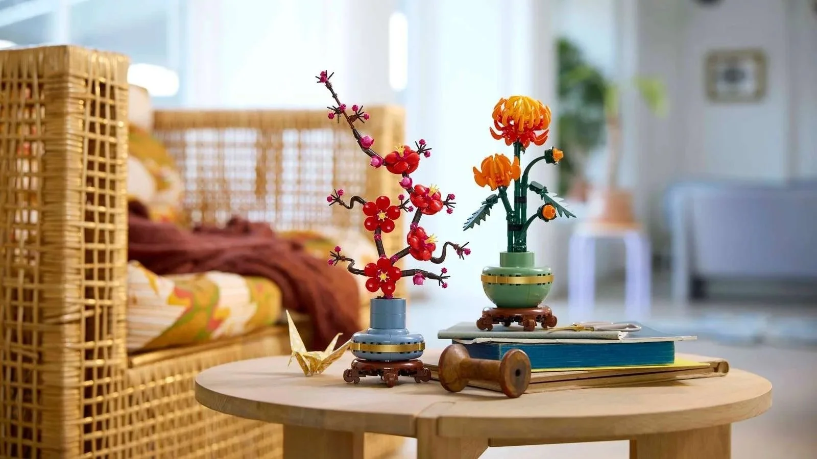 LEGO Plum Blossom and Chrysanthemum arrangements on a round wooden table with a stack of books and a paper crane
