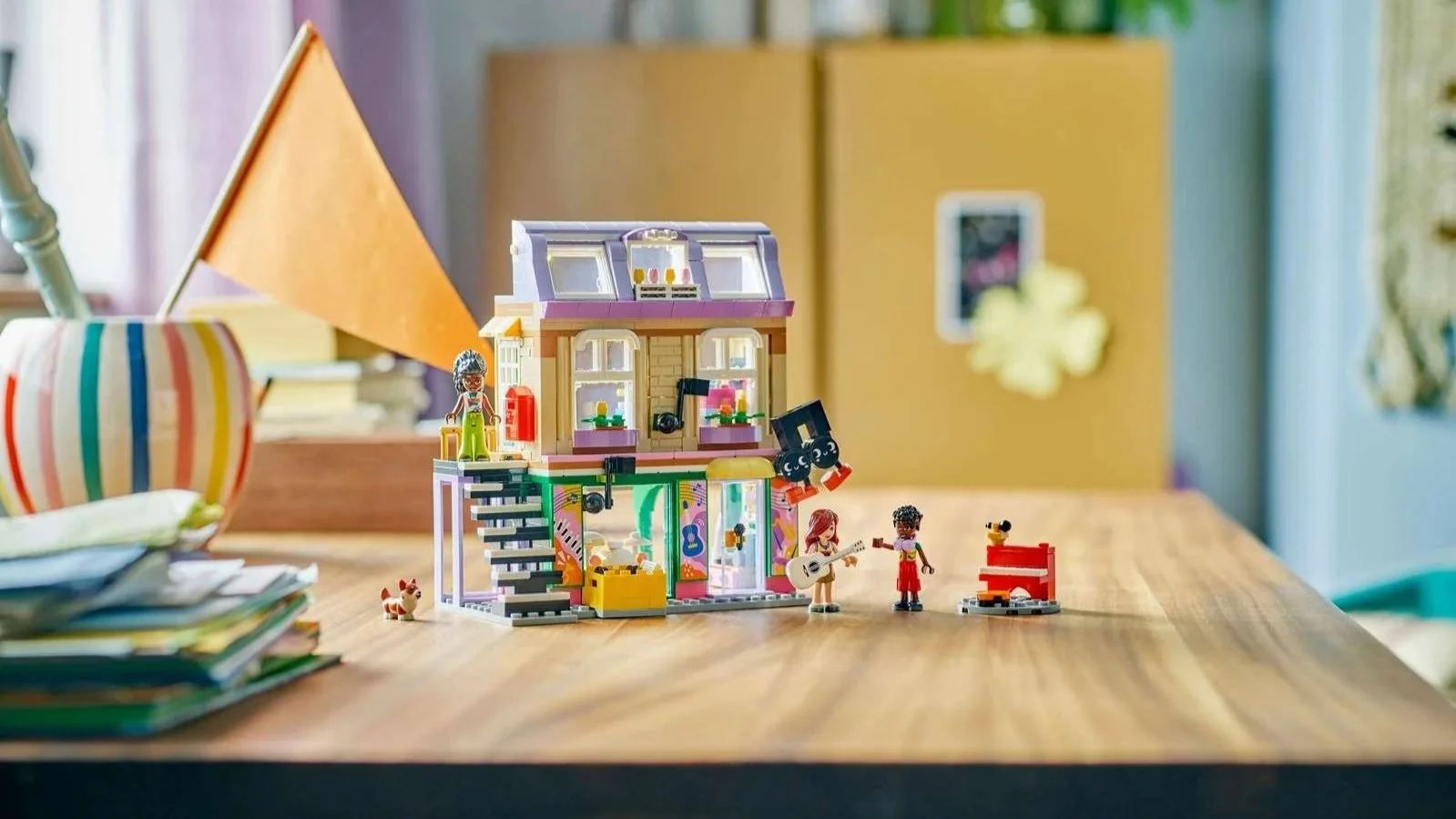 LEGO Music Store and Apartment set on a wooden desk, a two-story building with a purple roof, outdoor staircase and balcony, plus a figure with a guitar beside a red piano