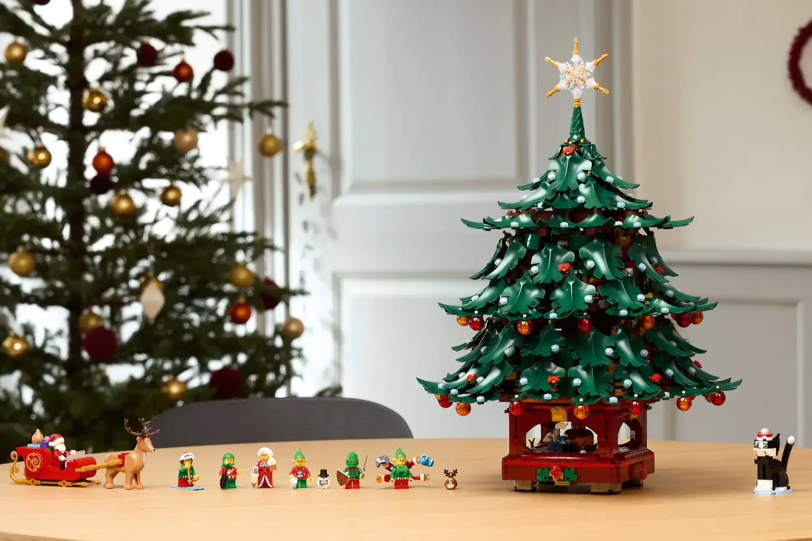 LEGO Family Christmas Tree with layered green branches, ornaments, and a snowflake star, beside Santa in a sleigh, a reindeer, elves, and a cat