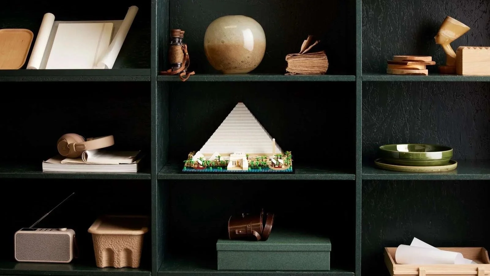 LEGO Great Pyramid of Giza set displayed on a dark green bookshelf beside ceramics and a Nefertiti bust