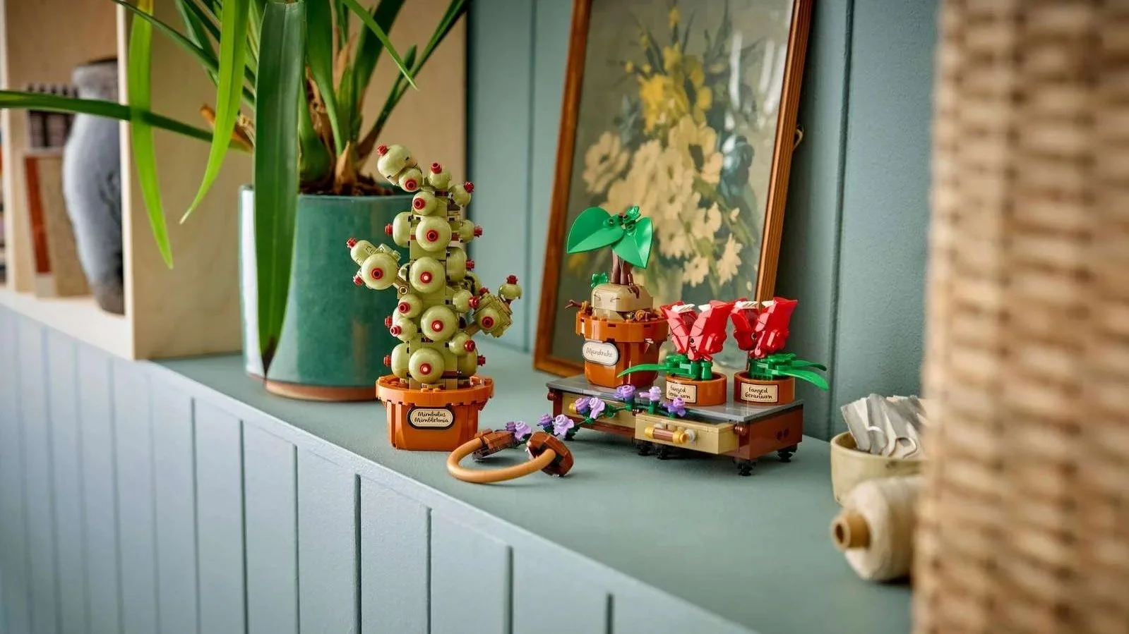 LEGO Hogwarts Herbology Plants set with a Mimbulus Mimbletonia, a mandrake and two fanged geraniums on a shelf beside a floral painting