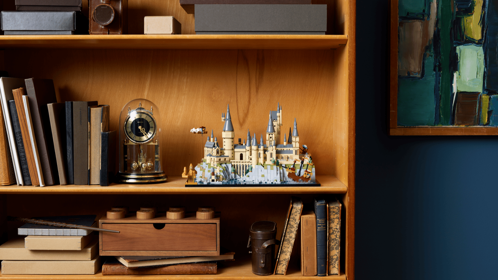 LEGO Hogwarts Castle and Grounds set displayed on a wooden bookshelf next to an antique clock and leather-bound books
