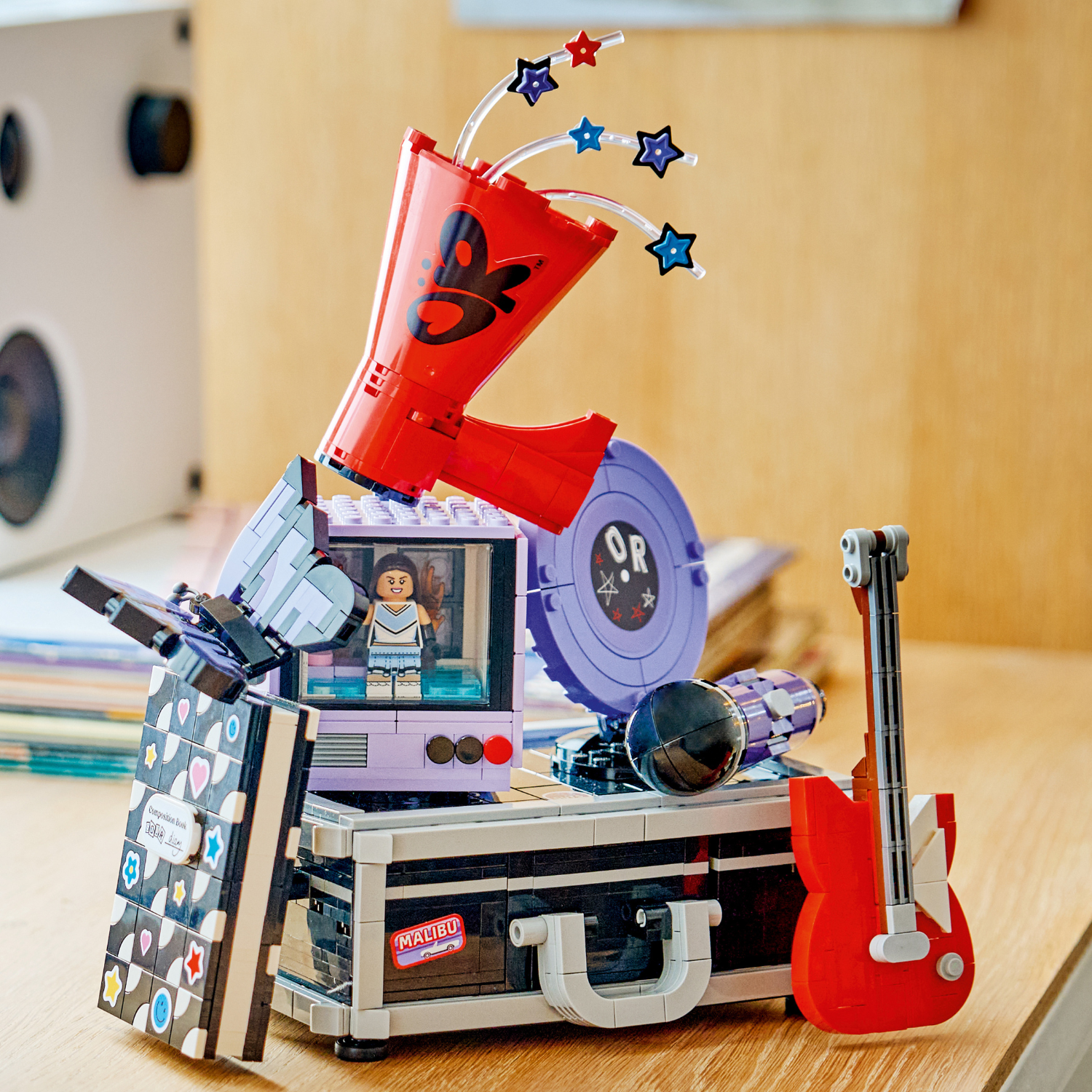 LEGO Olivia Rodrigo’s Secret Storage set: a black suitcase topped with a purple retro TV, minifigure, red megaphone, guitar and microphone