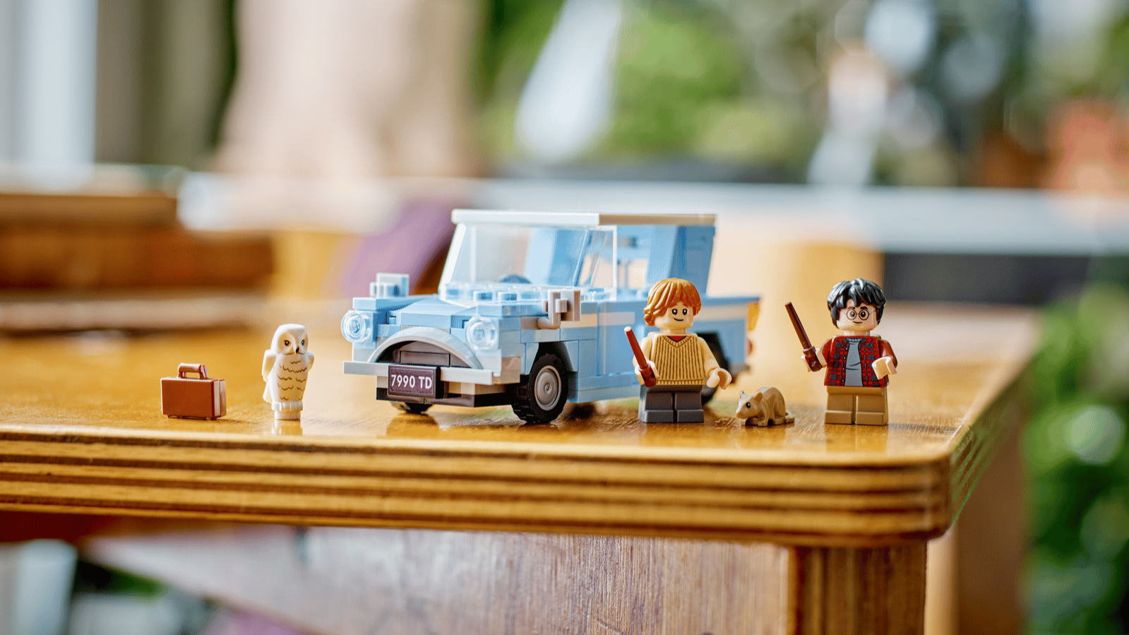 LEGO Harry Potter Flying Ford Anglia set in light blue with Harry and Ron minifigures, Hedwig the owl and a brown suitcase on a wooden table