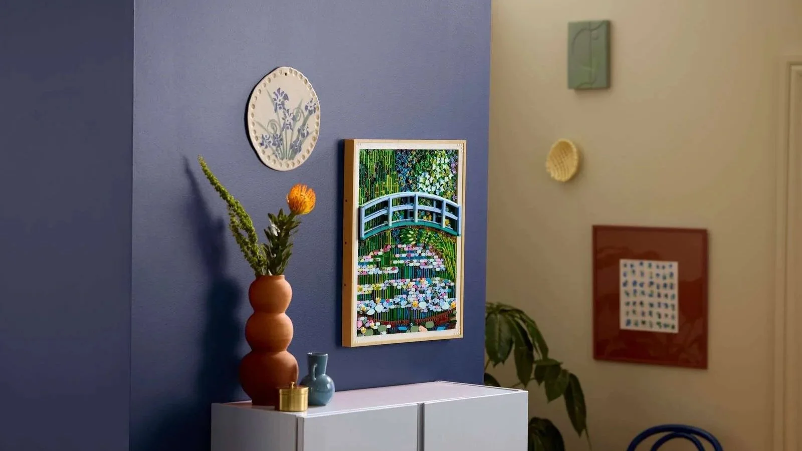 LEGO Art Claude Monet Bridge over a Pond of Water Lilies set displayed on a navy wall beside a ceramic iris plate