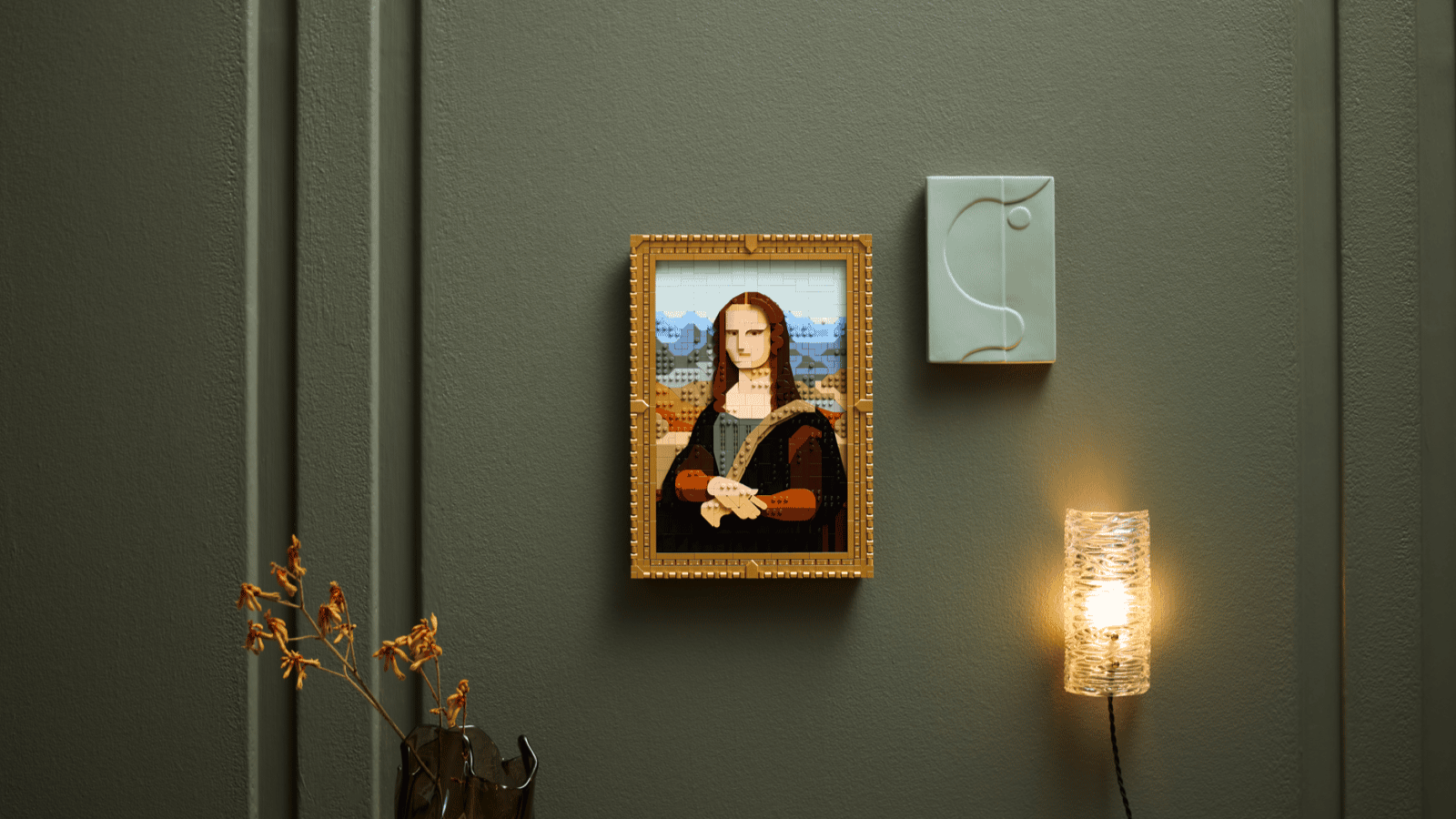 LEGO Mona Lisa set in a gold brick frame on a dark green paneled wall beside a glowing sconce