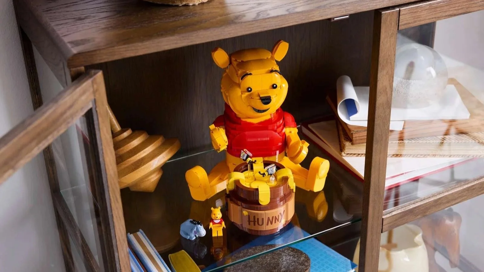 LEGO Winnie the Pooh set sitting beside a brick-built honey pot inside a glass display cabinet