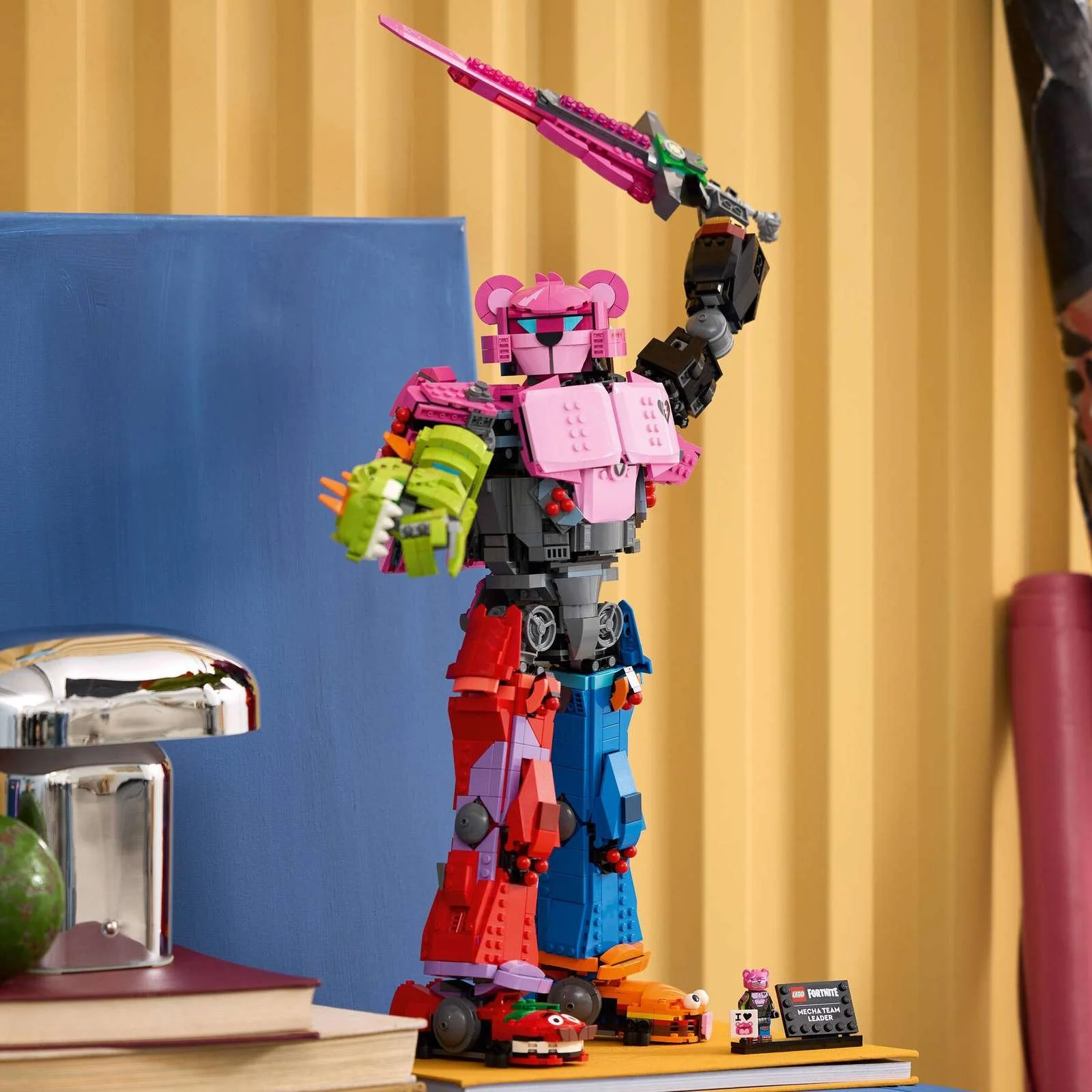LEGO Fortnite Mecha Team Leader set, a pink and blue robot figure holding a sword, positioned beside a chrome lamp and books