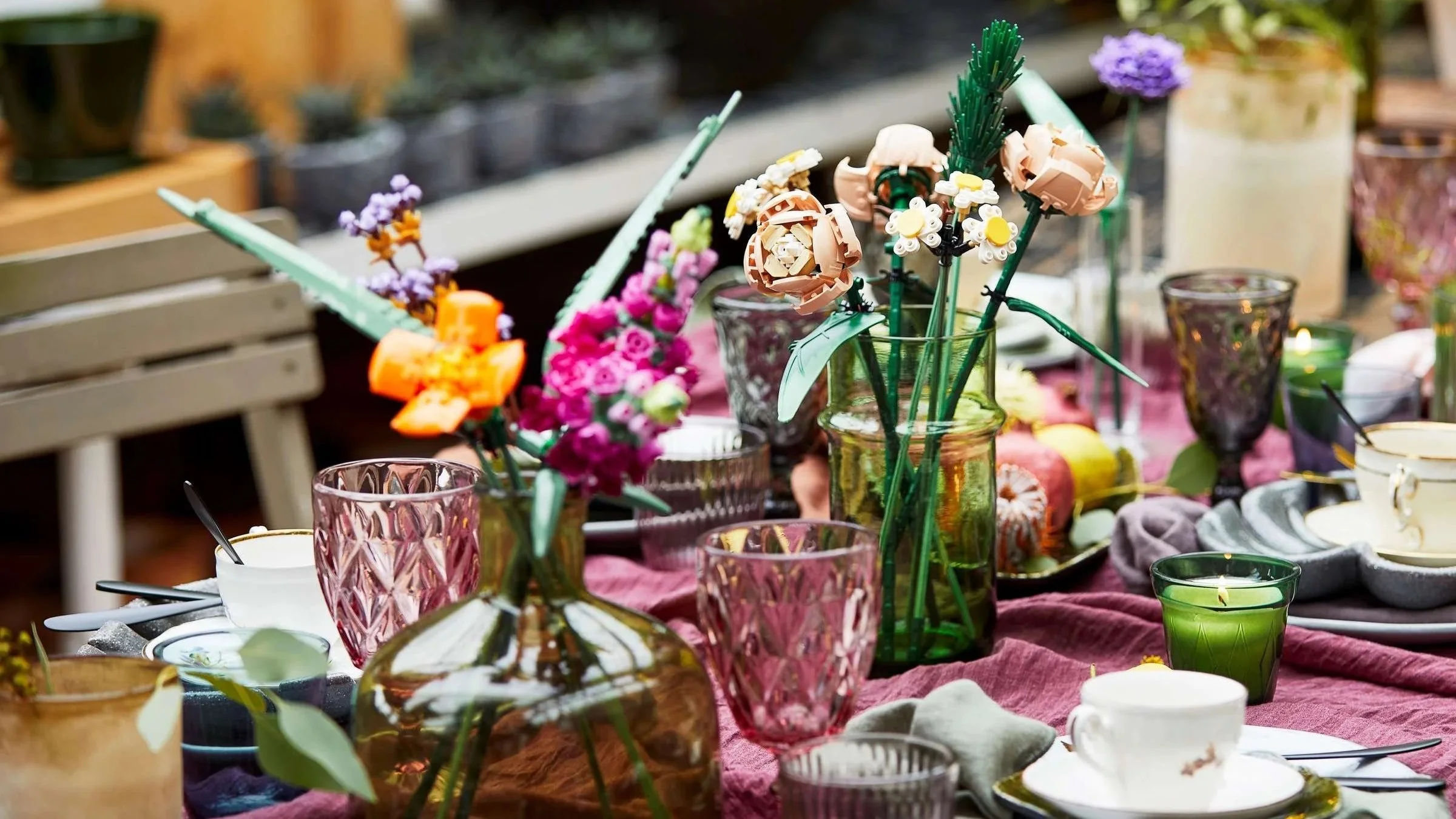 Assorted LEGO flowers in colored glass vases styled as a centerpiece on an outdoor table with a pink linen runner