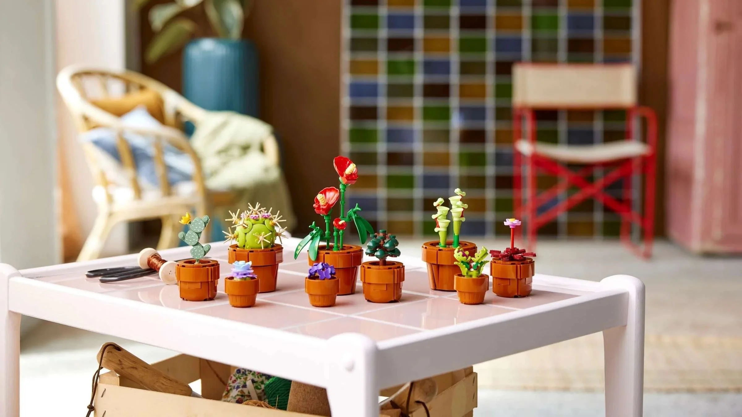 LEGO Tiny Plants set of small potted cacti and flowers displayed across a tiled side table, with a woven chair in the background