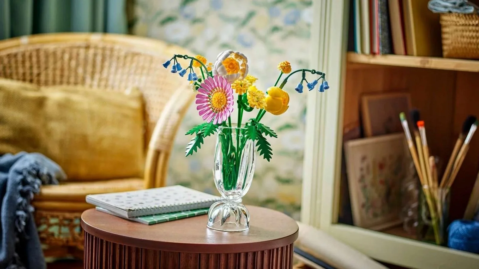 LEGO Petite Sunny Bouquet set in a small glass vase on a round wooden side table next to a wicker armchair