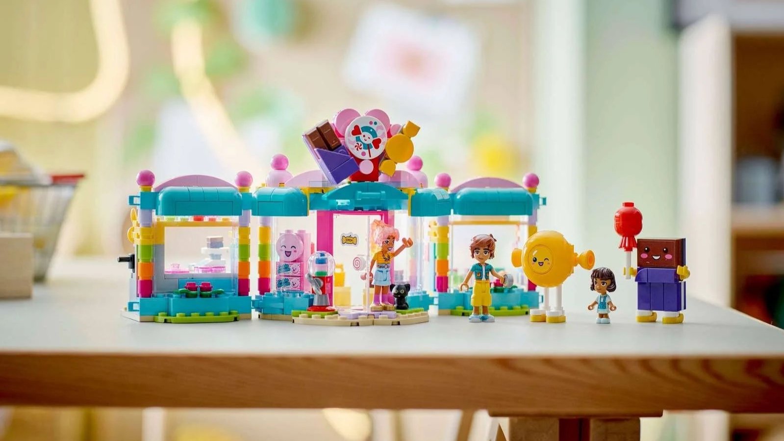 LEGO Heartlake City Candy Store set on a wooden desk, a pastel shop with teal awnings and a big candy sign, three figures, a black cat and two candy characters