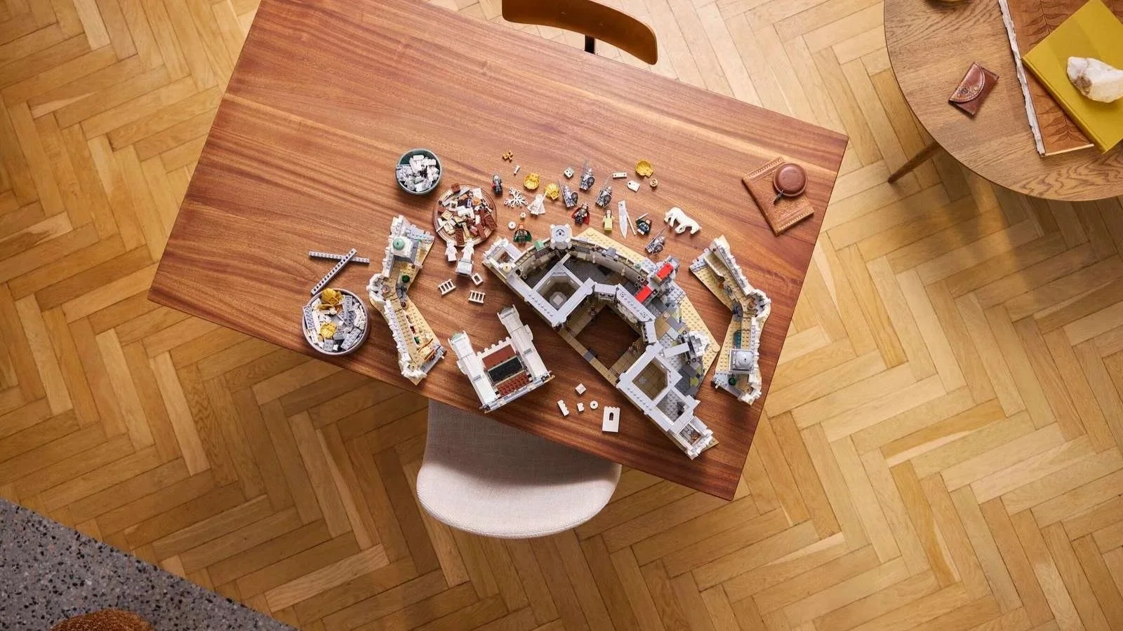 Unfinished LEGO Lord of the Rings Minas Tirith castle on a wooden table, with minifigures and pieces sorted in bowls