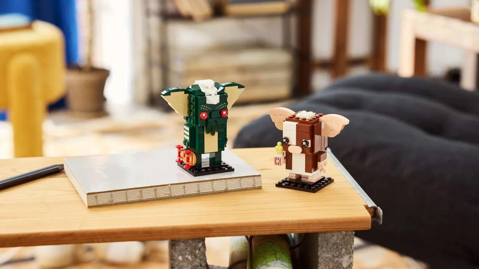 LEGO Gremlins Gizmo and Stripe figures side by side on a wooden table, Gizmo holding popcorn and Stripe with a skateboard