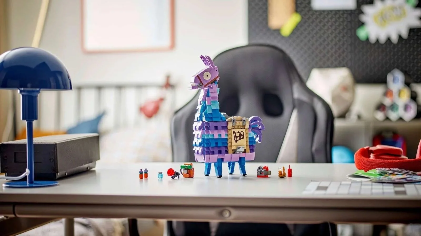 LEGO Fortnite Supply Llama set on a desk surrounded by tiny loot pieces, with a blue lamp and gaming chair behind it