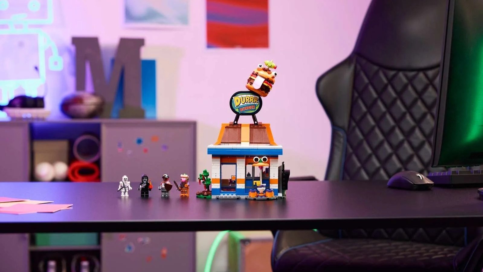 Fortnite Durrr Burger Restaurant LEGO set with a giant burger sign on the roof and minifigures in front, on a gaming desk