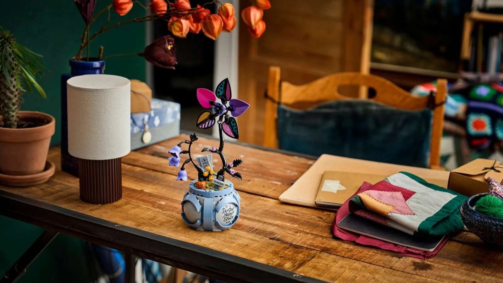LEGO Sally's Flowerpot set from The Nightmare Before Christmas on a rustic wooden desk beside a lamp and notebooks
