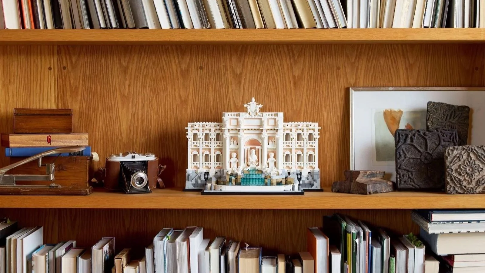 LEGO Trevi Fountain set styled on a warm wood bookshelf between vintage books and an old film camera