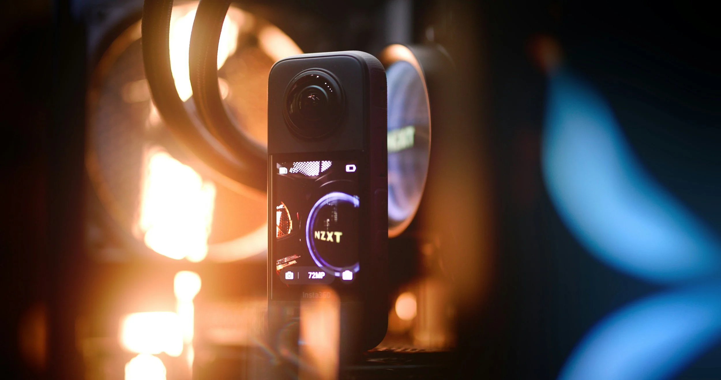 A close-up of a smartphone mounted on a stabilizer or gimbal, displaying its camera interface with settings such as 72 megapixels and a battery icon, while the background features circular lights and a warm glow.
