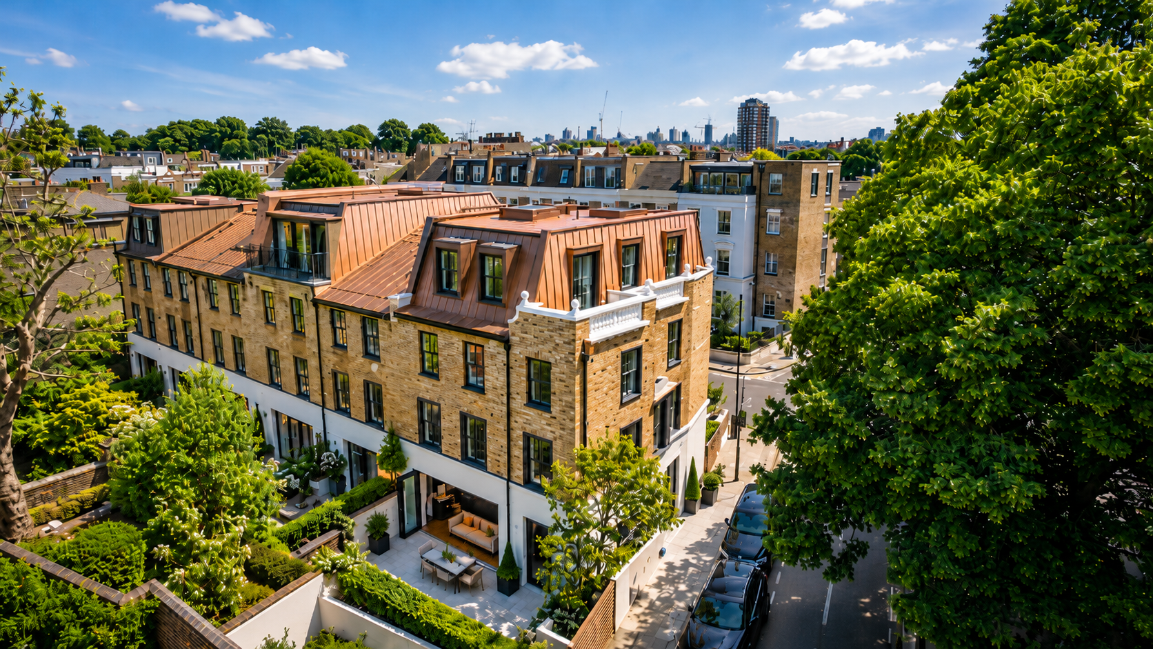 Aerial view of a city neighborhood with modern multi-story brick buildings, rooftop patios, and lush greenery, under a partly cloudy blue sky.
