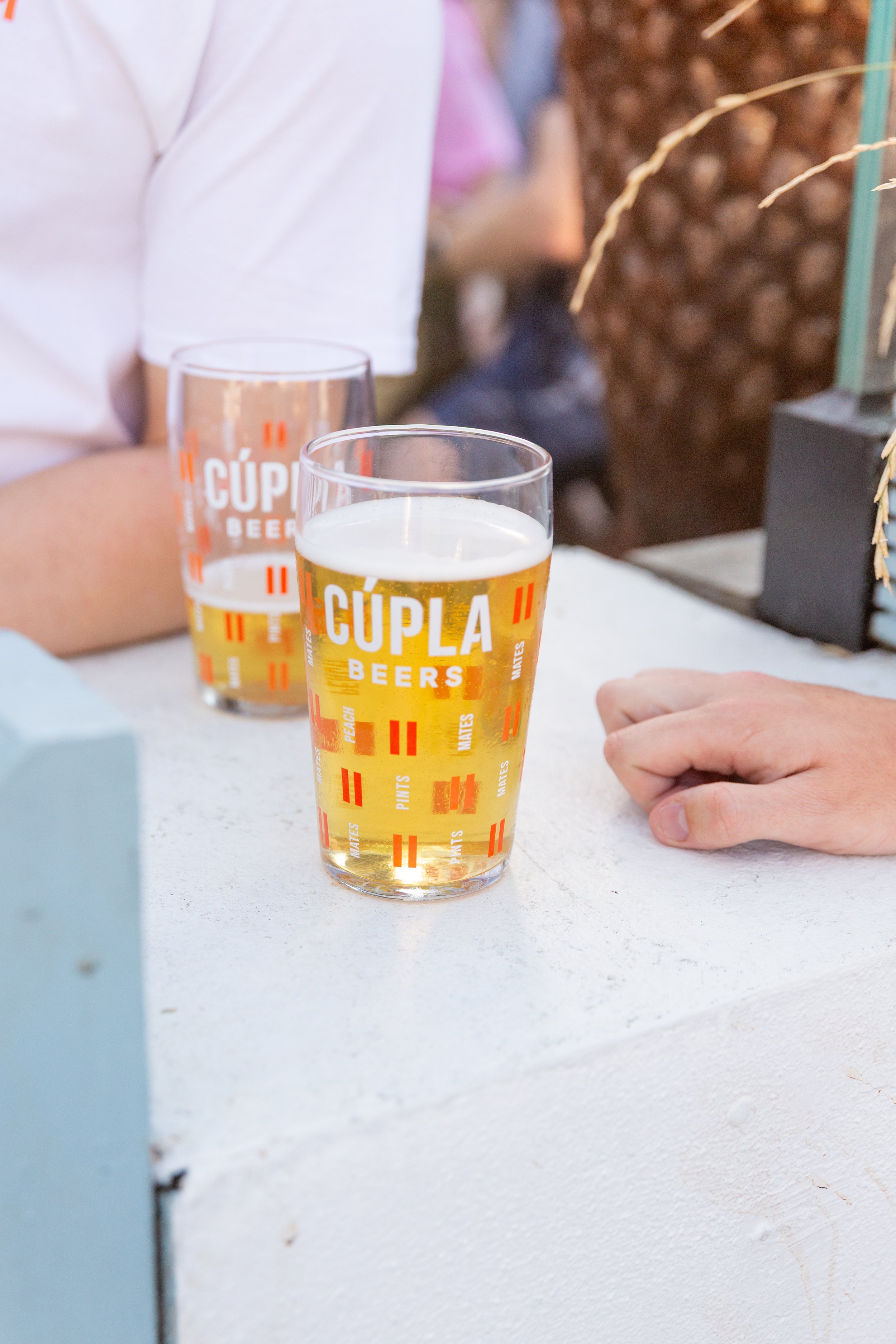 Cúpla Beers Branded Pint Glasses with Logo, Dual Line Motif, Mates, Pints and Peach text also on glass. One nearly empty and one nearly full pint of Cúpla Peach in each.