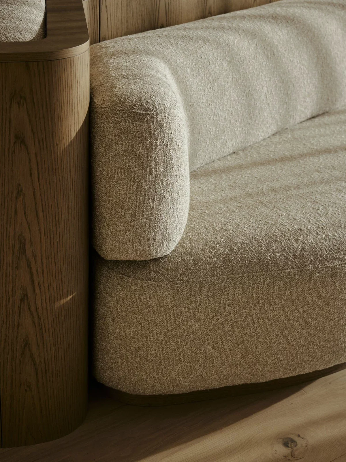 Close-up of a beige textured upholstered sofa next to a wooden wall and a round wooden side table.