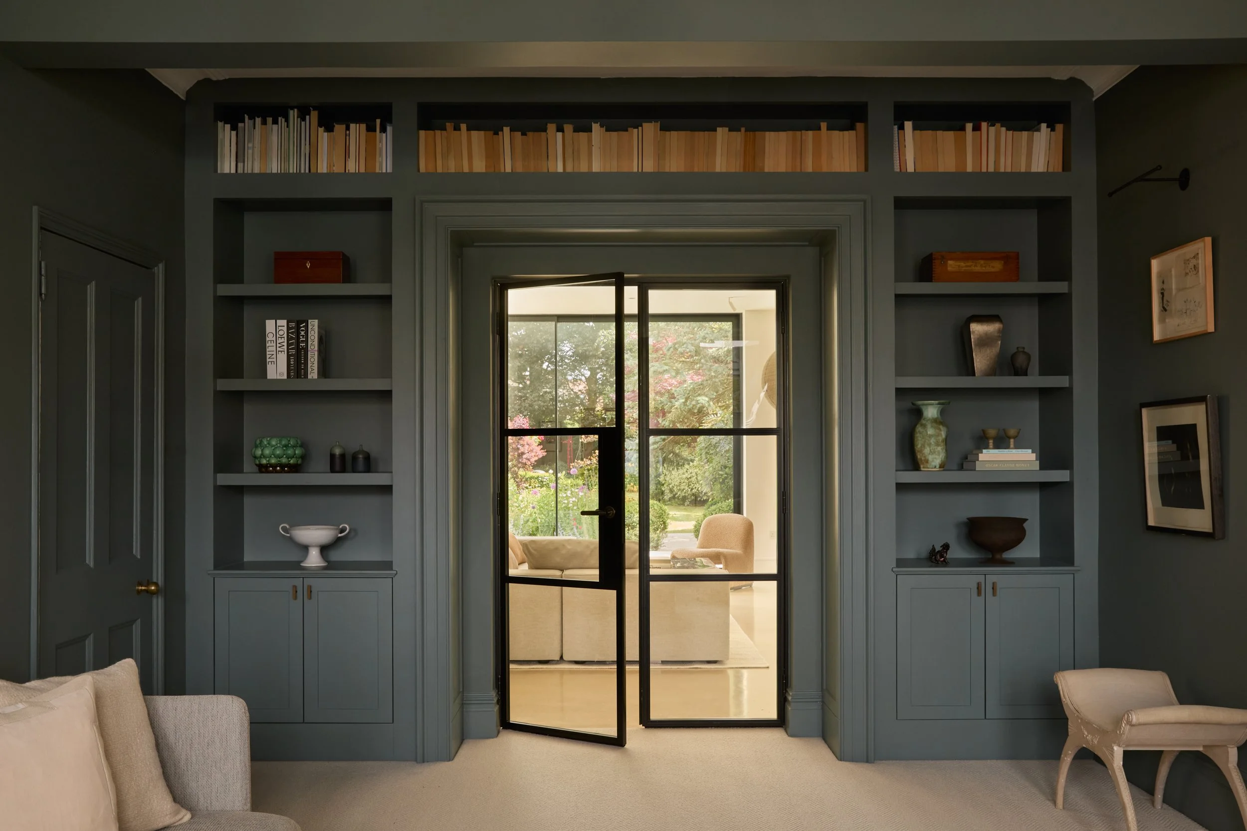 Living room with painted blue walls, built-in shelves with books and decorative items, glass-paned black door leading outside, and beige furniture.