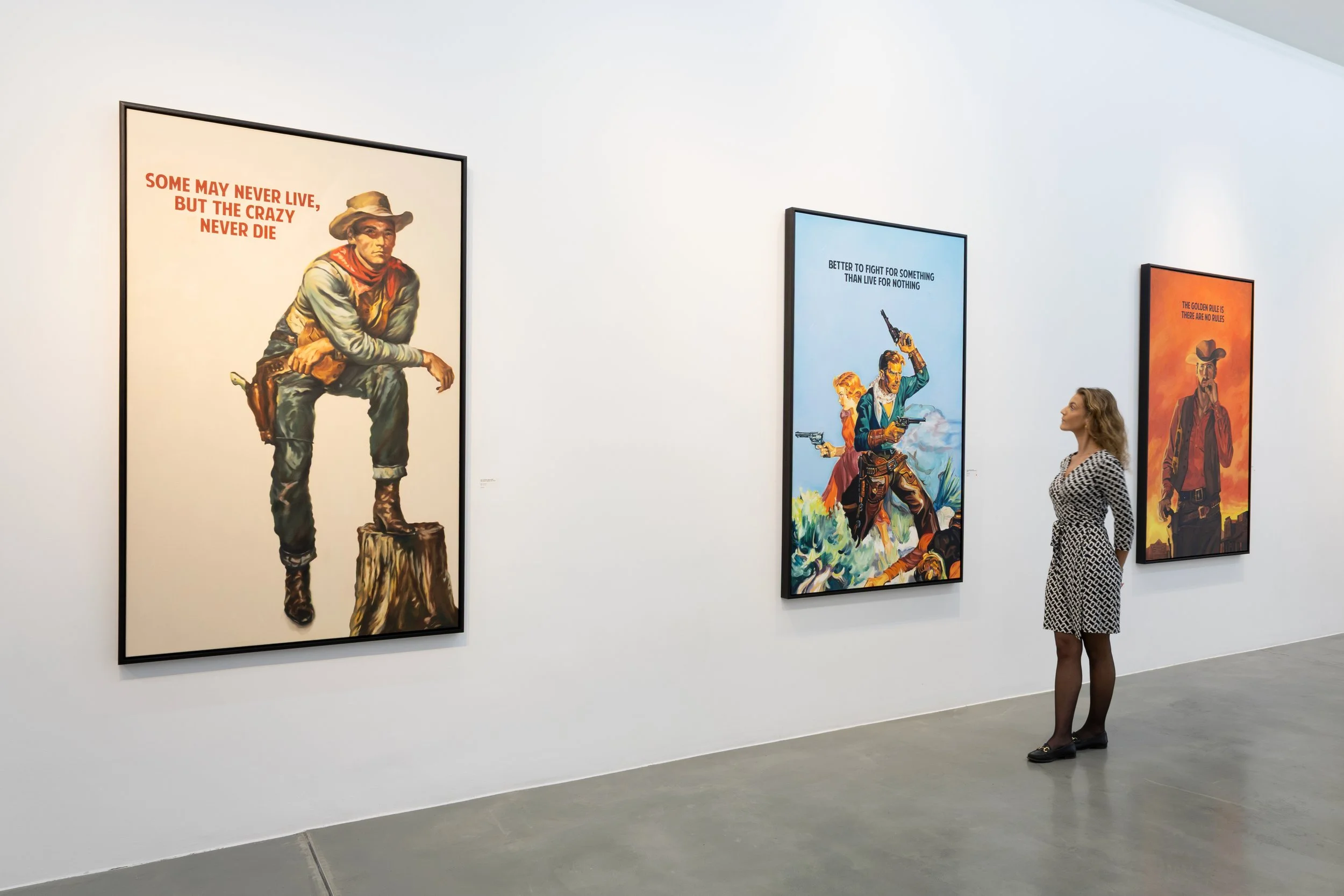 A woman in a patterned dress looking at framed artwork in a gallery with white walls.