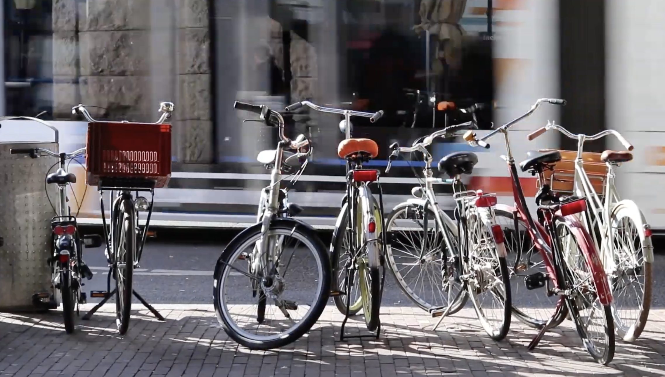 Row of bicycles parked on a sidewalk with a building in the background.