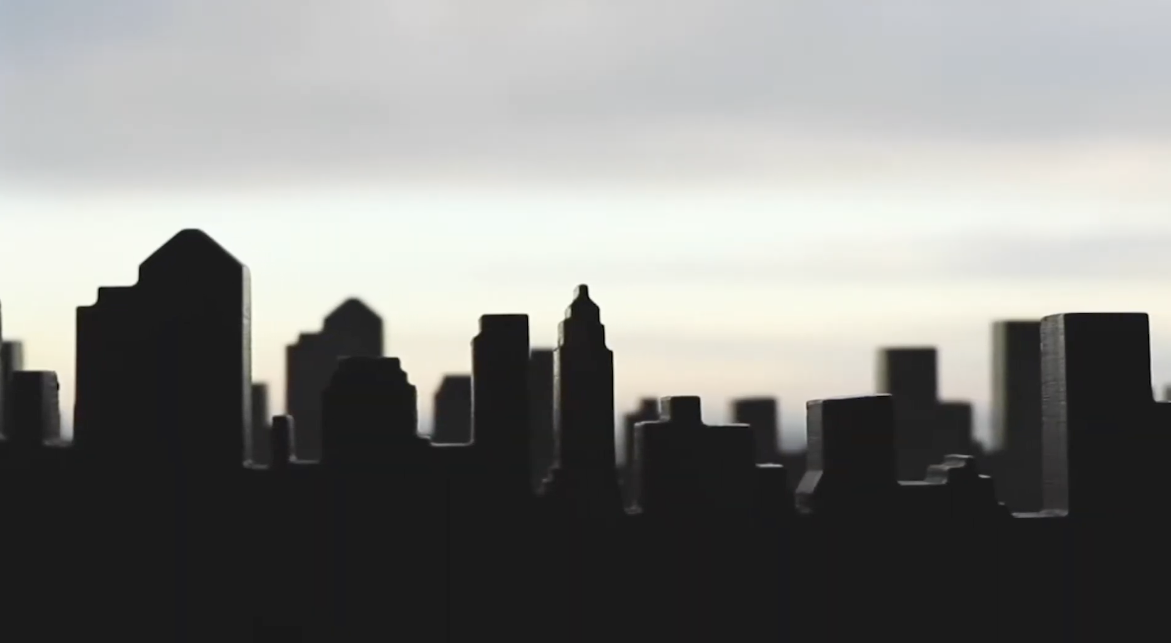 Silhouette of a city skyline with tall buildings against a cloudy sky during dusk or dawn.