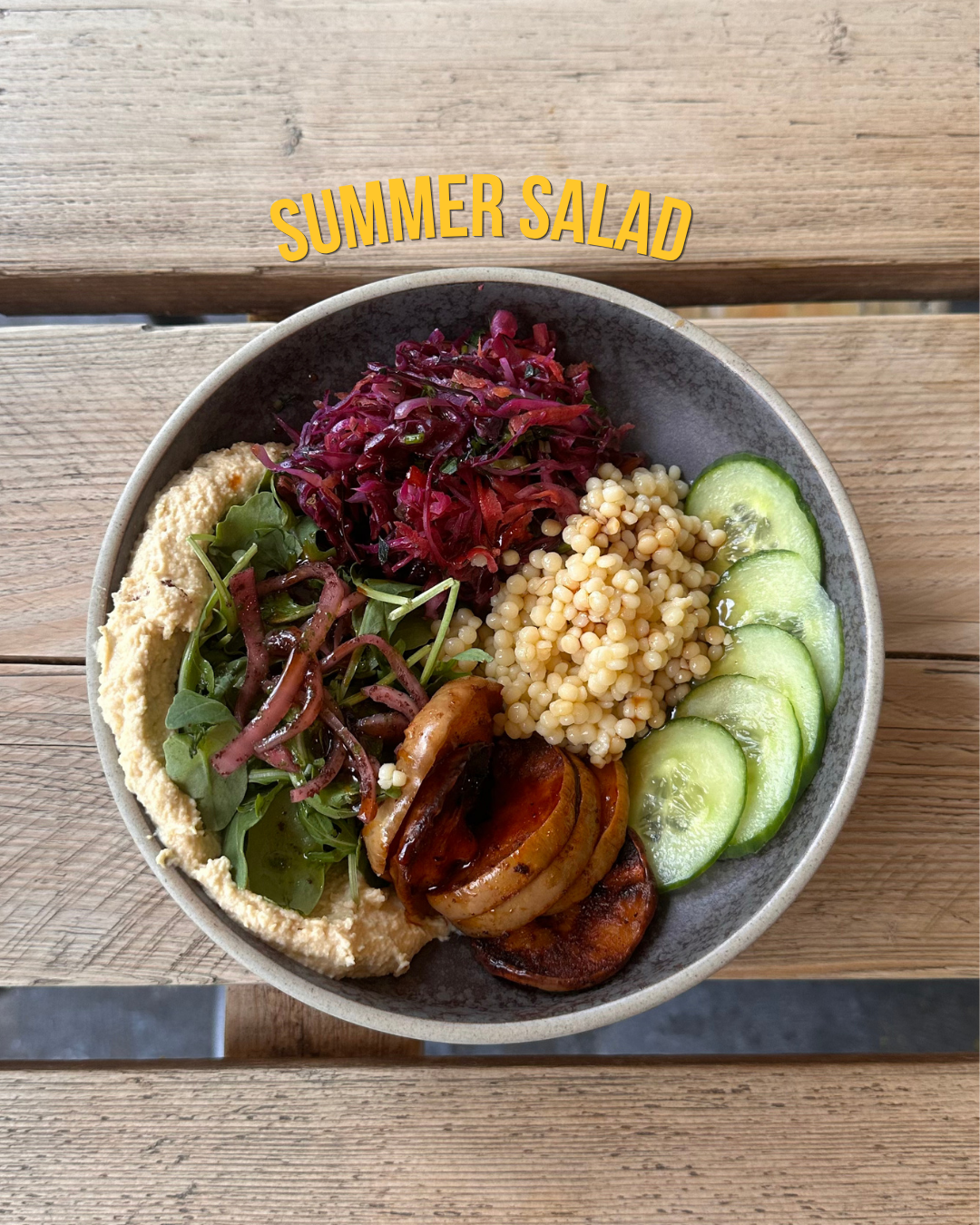A bowl of summer salad containing sliced cucumbers, couscous, grilled onion, sautéed greens, shredded beets, and hummus, labeled as 'Summer Salad'.