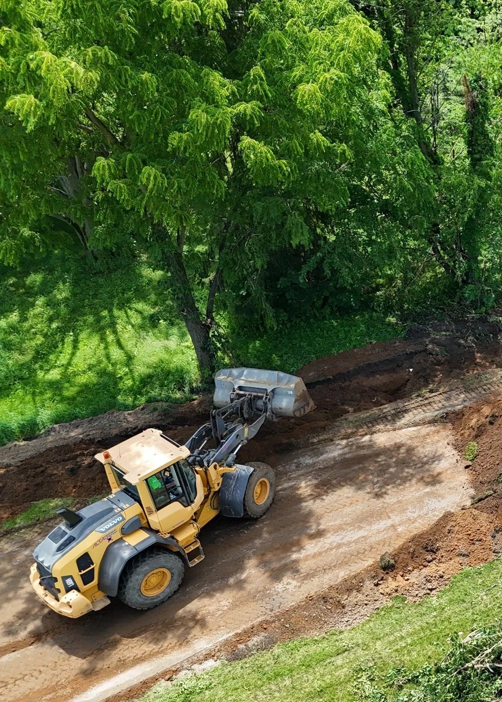 A yellow bulldozer moving dirt on a construction site surrounded by green trees and grass.