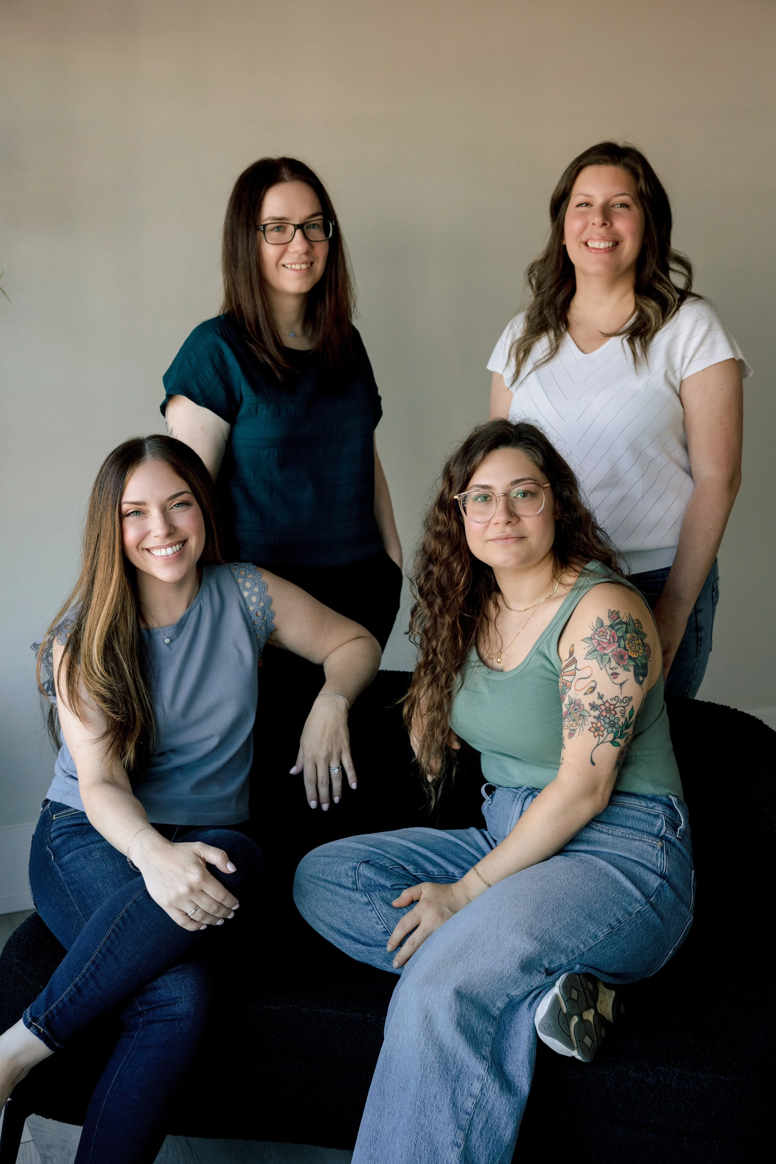 Group of four young women with diverse hair colors and styles, smiling and sitting against a neutral background.