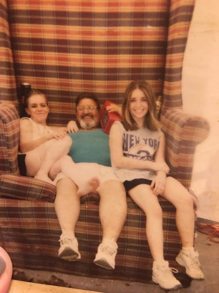 A man with two young girls sitting on a plaid couch and smiling at the camera.